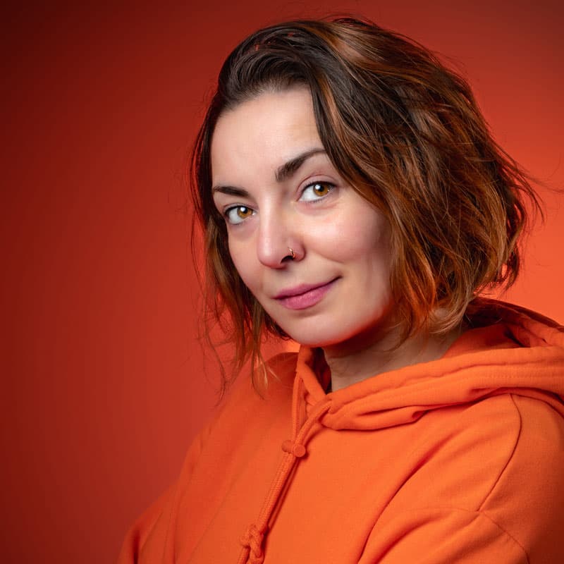 Portrait studio d'une jeune femme en sweat orange sur fond rouge